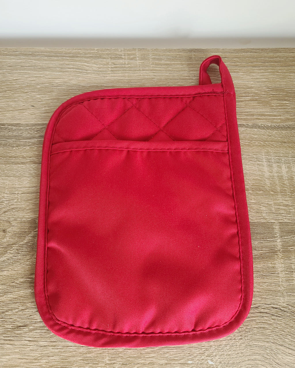 A single red quilted pot holder with a top loop handle, laid flat on a light wood surface.
