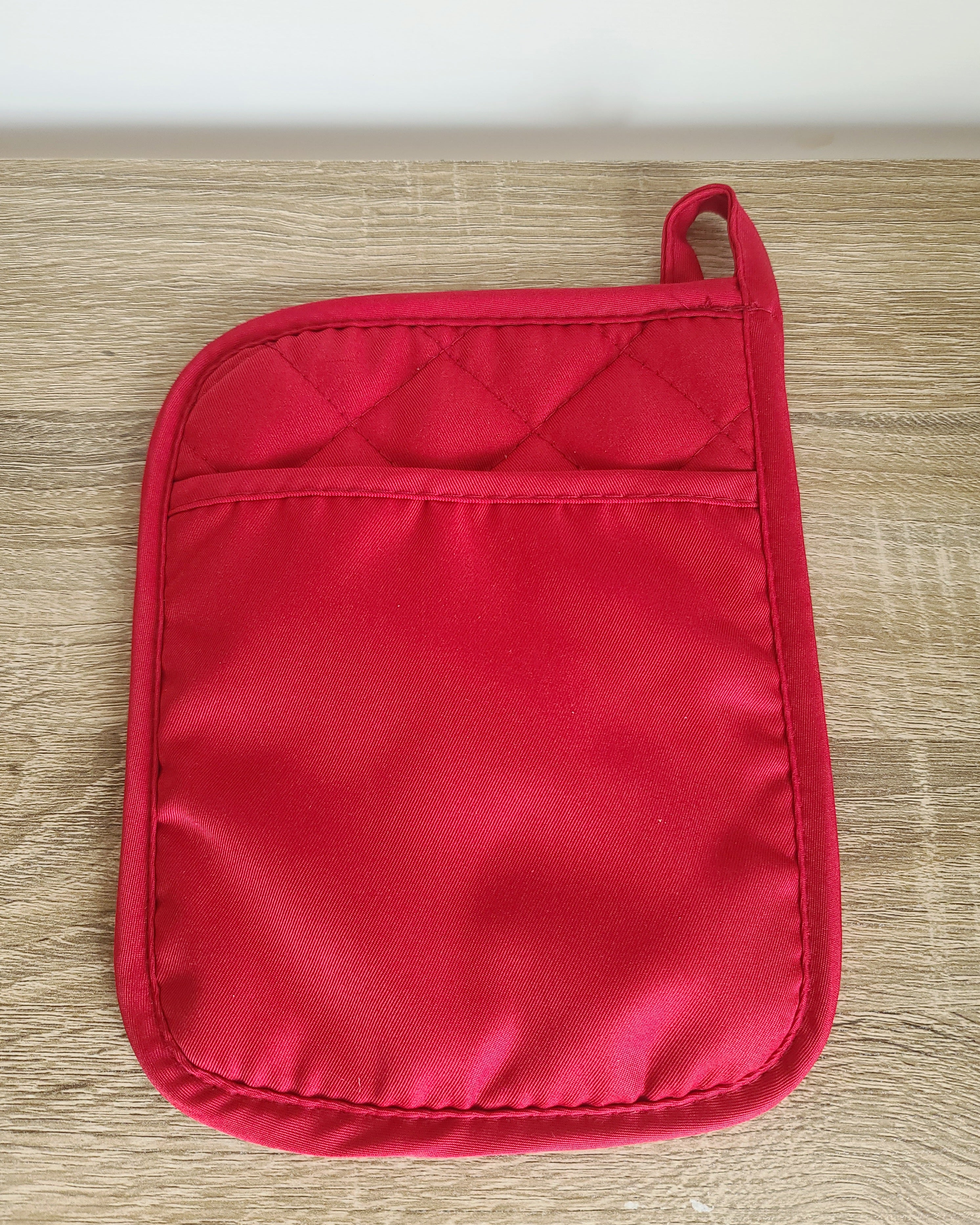 A single red quilted pot holder with a top loop handle, laid flat on a light wood surface.